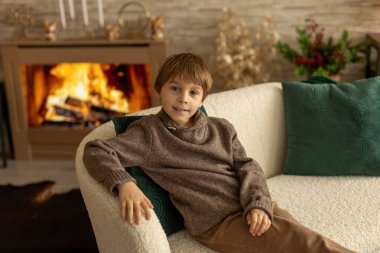 Hoş bir okul çocuğu, süslü bir odada oturuyor, kış dekorasyonu, şömine ve çiçekler, huzur ve sessizliğin tadını çıkarıyor.