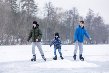 Mutlu çocuk, çocuk, sıradan giyinmiş, gün boyunca donmuş bir gölde paten kayıyor, ormanın arkasında güzel bir günbatımı, eğleniyor.