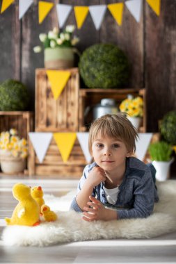 Sevimli bir anaokulu çocuğu, oğlum, evde ördeklerle oynuyor, arkasında doğum günü için güzel bir bahar süslemesi var.