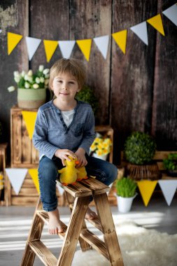 Sevimli bir anaokulu çocuğu, oğlum, evde ördeklerle oynuyor, arkasında doğum günü için güzel bir bahar süslemesi var.