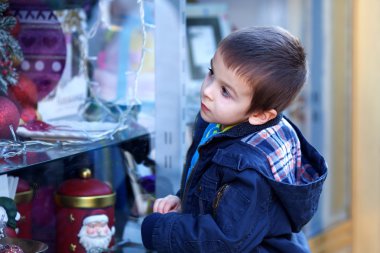 Sweet little boy, looking through a window in shop, decorated fo clipart