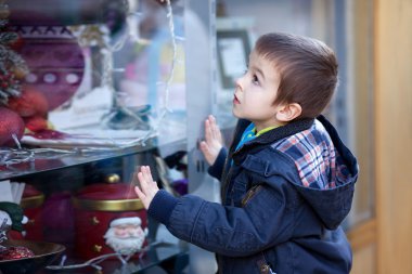Sweet little boy, looking through a window in shop, decorated fo clipart