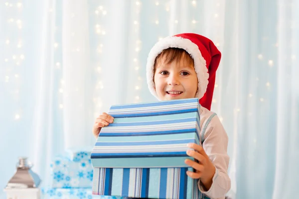 Χαμογελώντας αστείο παιδί στη Σάντα κόκκινο καπέλο κρατώντας χριστουγεννιάτικο δώρο σε h — Φωτογραφία Αρχείου