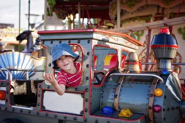 Cute boy on a merry-go-round carousel, riding a train — Stock fotografie