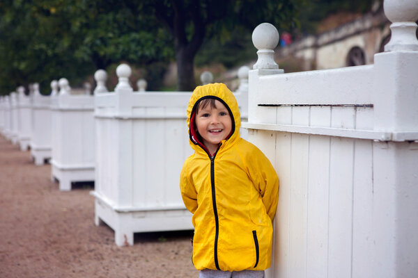 Cute boy in blooming garden, summertime on rainy day