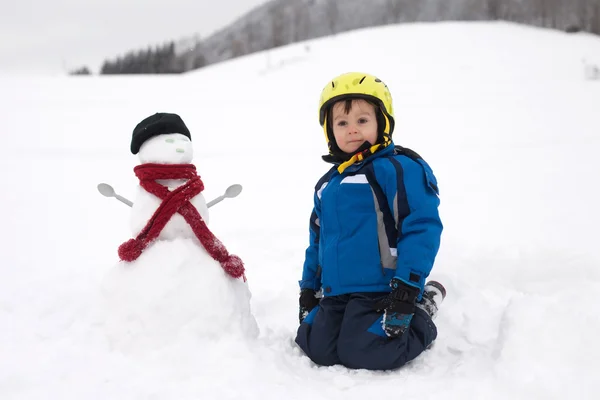 Menino feliz brincando na neve enquanto neva, capacete — Fotografia de Stock