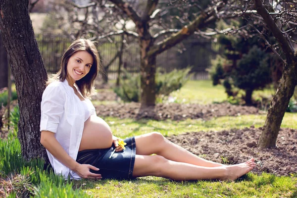 Ung gravid kvinna mot blommande träd på våren — Stockfoto