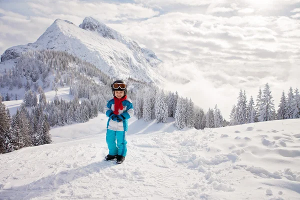 Adorable little boy with blue jacket and a helmet, skiing in win