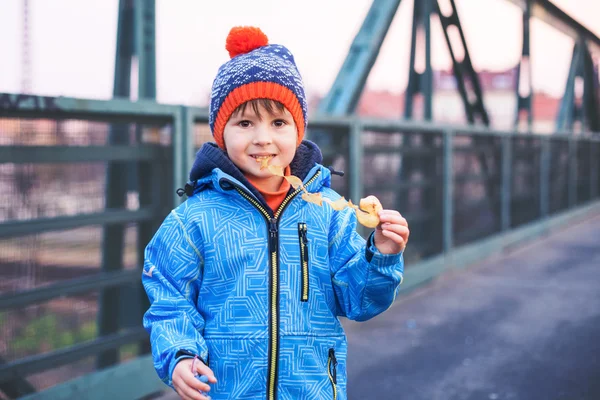 Lindo chico, comiendo papas fritas en un puente, al aire libre — Foto de Stock