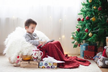 Sevimli küçük hasta çocuk, fasulye çanta, tablet üzerinde oynarken üzerinde oturan ve