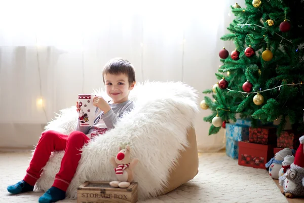 Niedlicher Junge, sitzt auf Bohnensack, trinkt Tee und genießt Weihnachten — Stockfoto