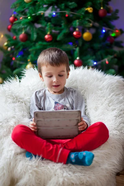 Cute little sick boy, sitting on bean bag, playing on tablet — Stock Photo, Image