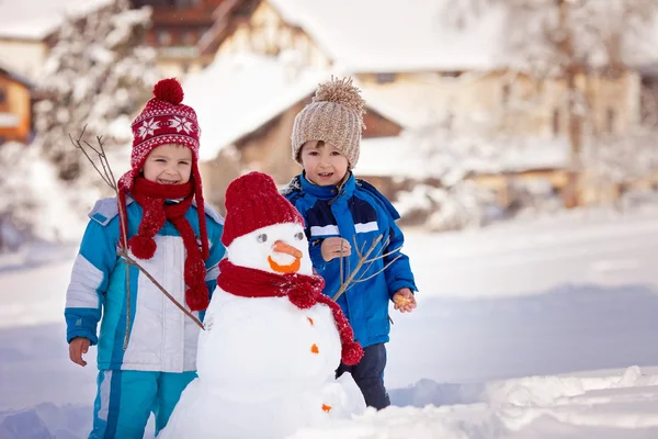 Feliz hermoso niños, hermanos, construcción de muñeco de nieve en el jardín — Foto de Stock
