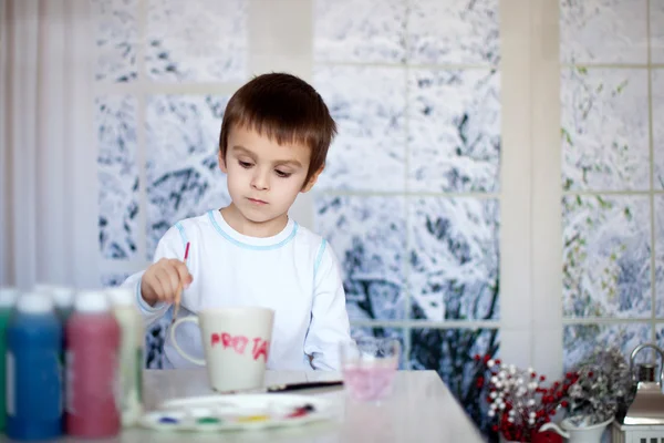 Carino piccolo bambino in età prescolare, disegno disegno su tazza per suo padre — Foto Stock