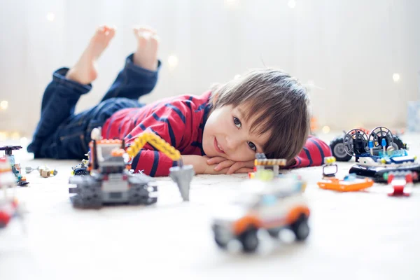 Pequeño niño jugando con un montón de juguetes de plástico de colores en interiores — Foto de Stock