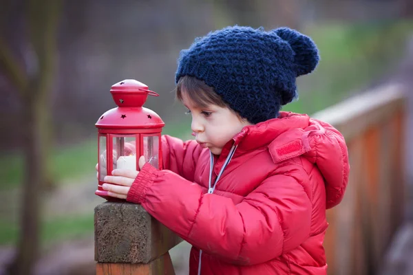 Dolce bambino, tenendo lanterna rossa nel parco in un inverno soleggiato d — Foto Stock