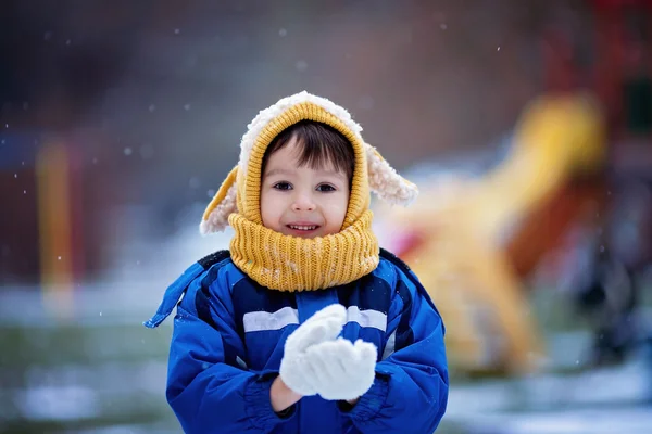 Niedlicher kleiner Junge, spielt mit Schnee im Park, Spielplatz — Stockfoto