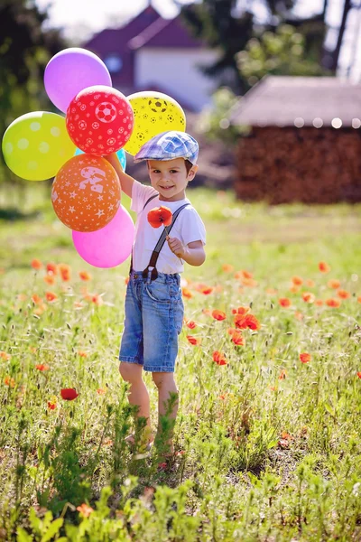 Niedlicher kleiner Junge mit Mohnblume auf Mohnfeld mit Luftballons — Stockfoto