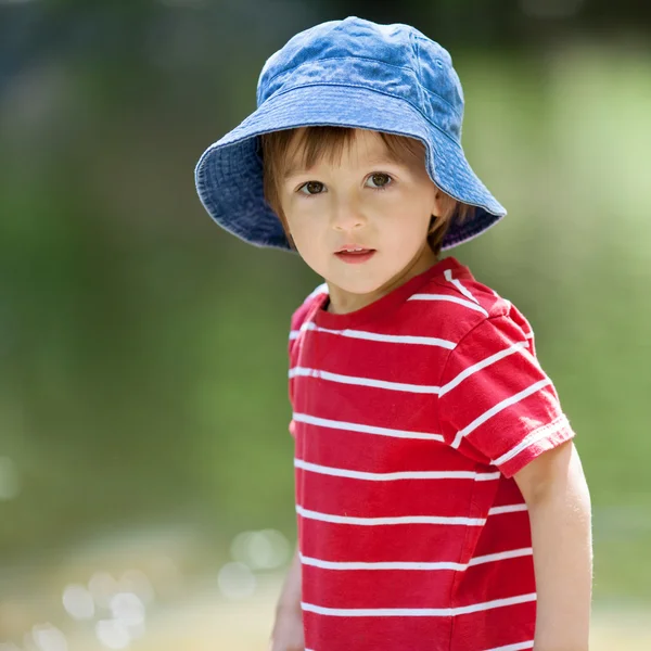 Portrait of a cute boy with summer hat on a edge of a river — Stock Photo, Image