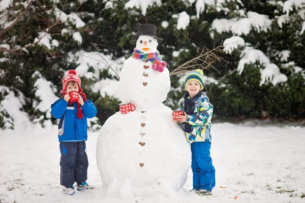 Feliz hermoso niños, hermanos, construcción de muñeco de nieve en el jardín —  Fotos de Stock