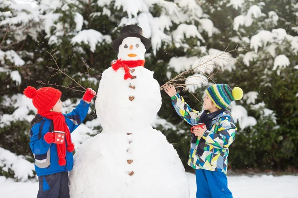 Feliz hermoso niños, hermanos, construcción de muñeco de nieve en el jardín —  Fotos de Stock