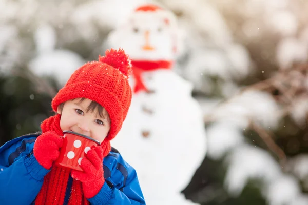 Feliz niño hermoso edificio muñeco de nieve en el jardín, tiempo de invierno, h — Foto de Stock