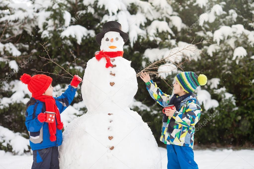 Happy beautiful children, brothers, building snowman in garden