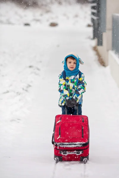 Симпатичный маленький мальчик с рюкзаком и чемоданом, собирается на лыжный отдых — стоковое фото