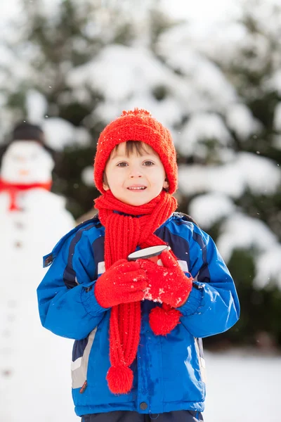 Criança bonita feliz construindo boneco de neve no jardim, tempo de inverno — Fotografia de Stock