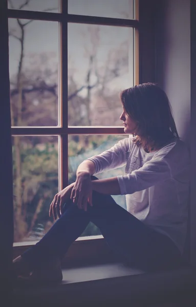 Junge attraktive Frau sitzt auf einem Fenster und schaut nach draußen — Stockfoto