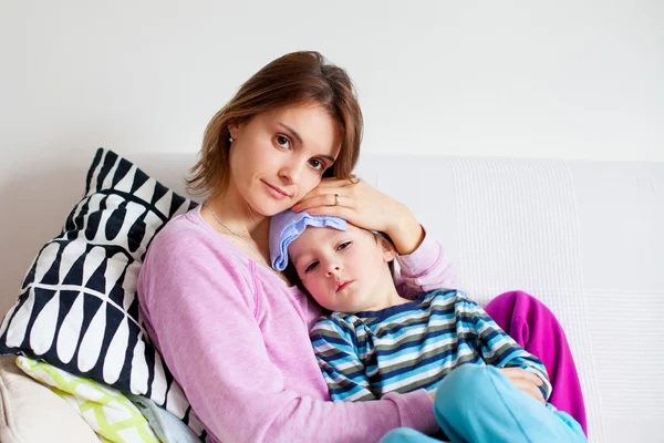 Young mother, holding her little sick boy, wet cloth on his fore — Stock Photo, Image