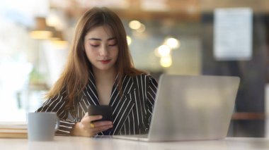 Ofis odasında dizüstü bilgisayarla çalışırken akıllı telefon kullanan kadınların cam duvarından bak 