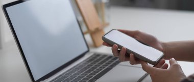 Dizüstü bilgisayarla çalışan beyaz masadaki akıllı telefonları kullanarak kadın elleri yan görünümü 