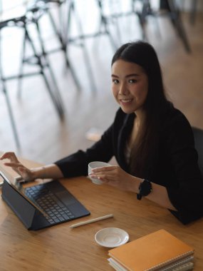 İş kadını portresi dijital tablet ve kırtasiyeyle çalışırken kahve molası verir. 