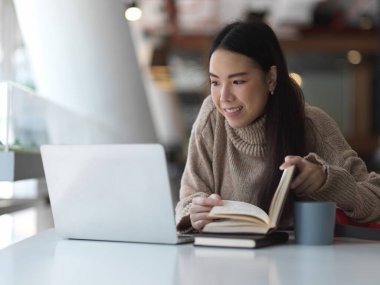 Süveter giyen bir kadının portresi. Laptop ve kitaplarla kafe 'de ödev yapıyor.