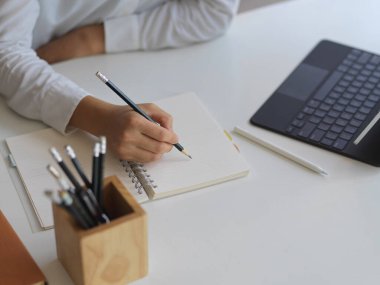 Ofis masasında kalemle boş bir deftere kadın eli yazarken çekilmiş bir kare.