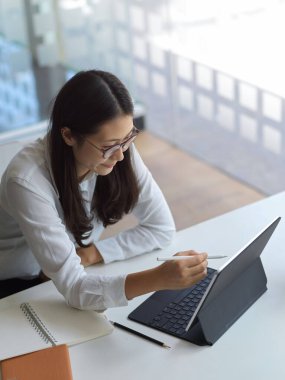 Çalışma alanında tablet kullanırken genç bir iş kadınının projesi üzerinde çalışırken görüntüsü kesildi.