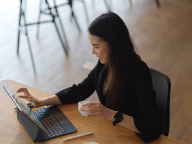 Ofiste elinde kahve fincanı tutarken dijital tabletle çalışan iş kadınının portresi