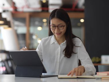 Ofis odasında tablet ve kırtasiyeyle çalışan kadın ofis çalışanının portresi.