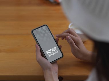 Akıllı telefon kullanan bir kadının yukarıdan çekilen görüntüleri arasında ahşap masa üzerindeki kesme yolunu da içeriyor