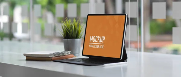 Side view of worktable with clipping path tablet, keyboard, notebooks and plant pot in glass wall office