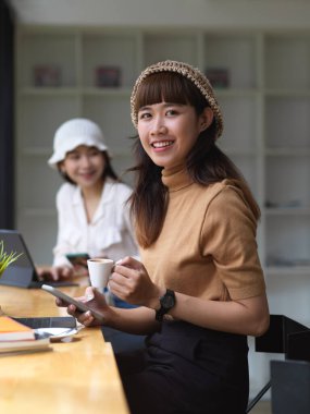 İki kız öğrencinin portresi kahve içerken kafede dijital tabletlerle ödevlerini yapıyorlar.