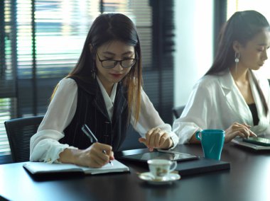 Ekibiyle toplantı odasında buluşurken not alan kadın ofis çalışanının portresi.