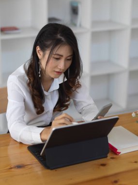 Akıllı telefonunda bilgi ararken tabletle çalışan genç bir ofis çalışanı. 