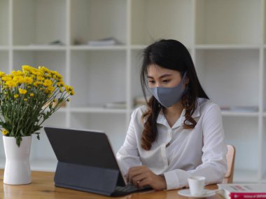 Maske takan ve ofis odasında dijital tabletle çalışan kadın portresi