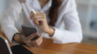 Ofis odasında akıllı telefonunu kullanan bir iş kadınının yakın plan görüntüsü. 