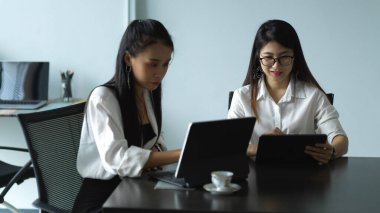 Toplantı odasında tabletle işlerine danışmanlık yapan iki kadın işçinin portresi.