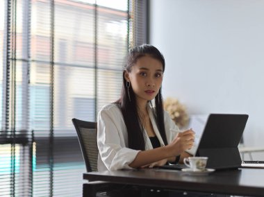 Ofiste tabletle çalışırken kameraya bakan kadın ofis çalışanının portresi.