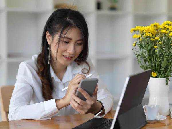 Tabletle çalışırken akıllı telefonunu kullanan genç ve güzel bir iş kadını. 