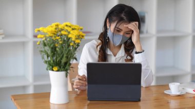 Maske takan ve tahta masa üzerinde dijital tabletle çalışan kadın işçilerin portresi